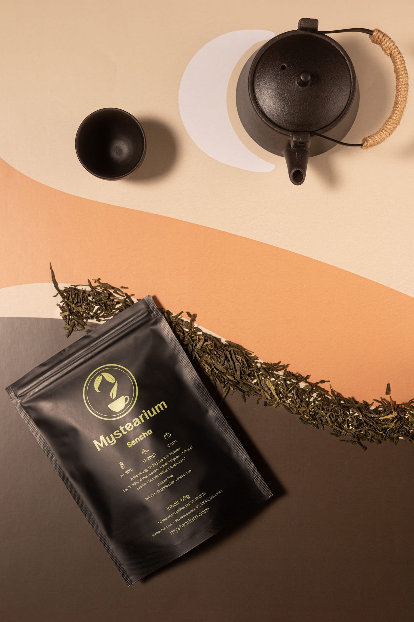 Black tea bag with 'Mysterialum' branding on a brown surface with a teapot and tea leaves.