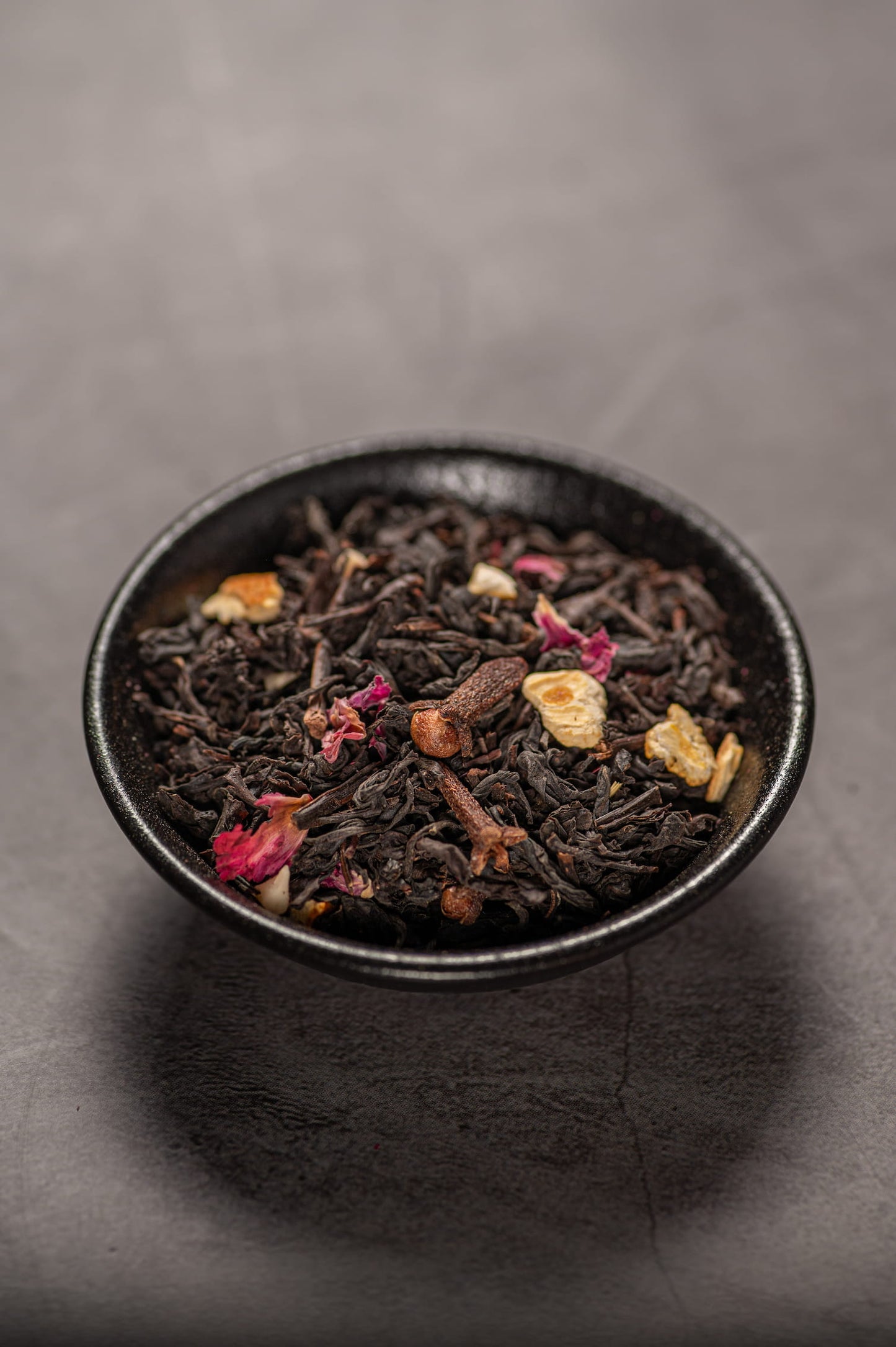 A black bowl filled with dry black tea with different spices and dried fruits.