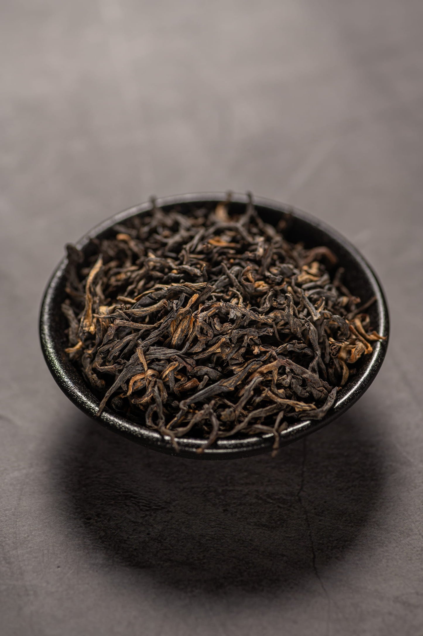 A black bowl filled with dry dianhong black tea.