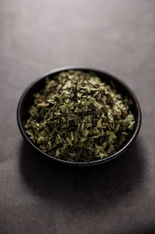 A bowl filled with a dry green tea blend called ‘Green Tea Mint,’ made from finely cut green tea leaves and dried mint leaves.