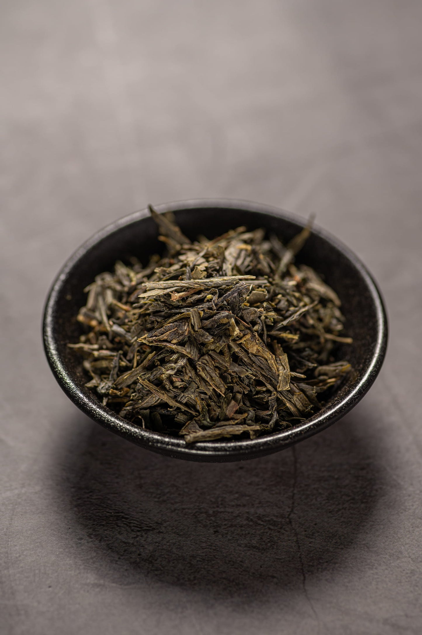 A black bowl filled with dry sencha green tea.
