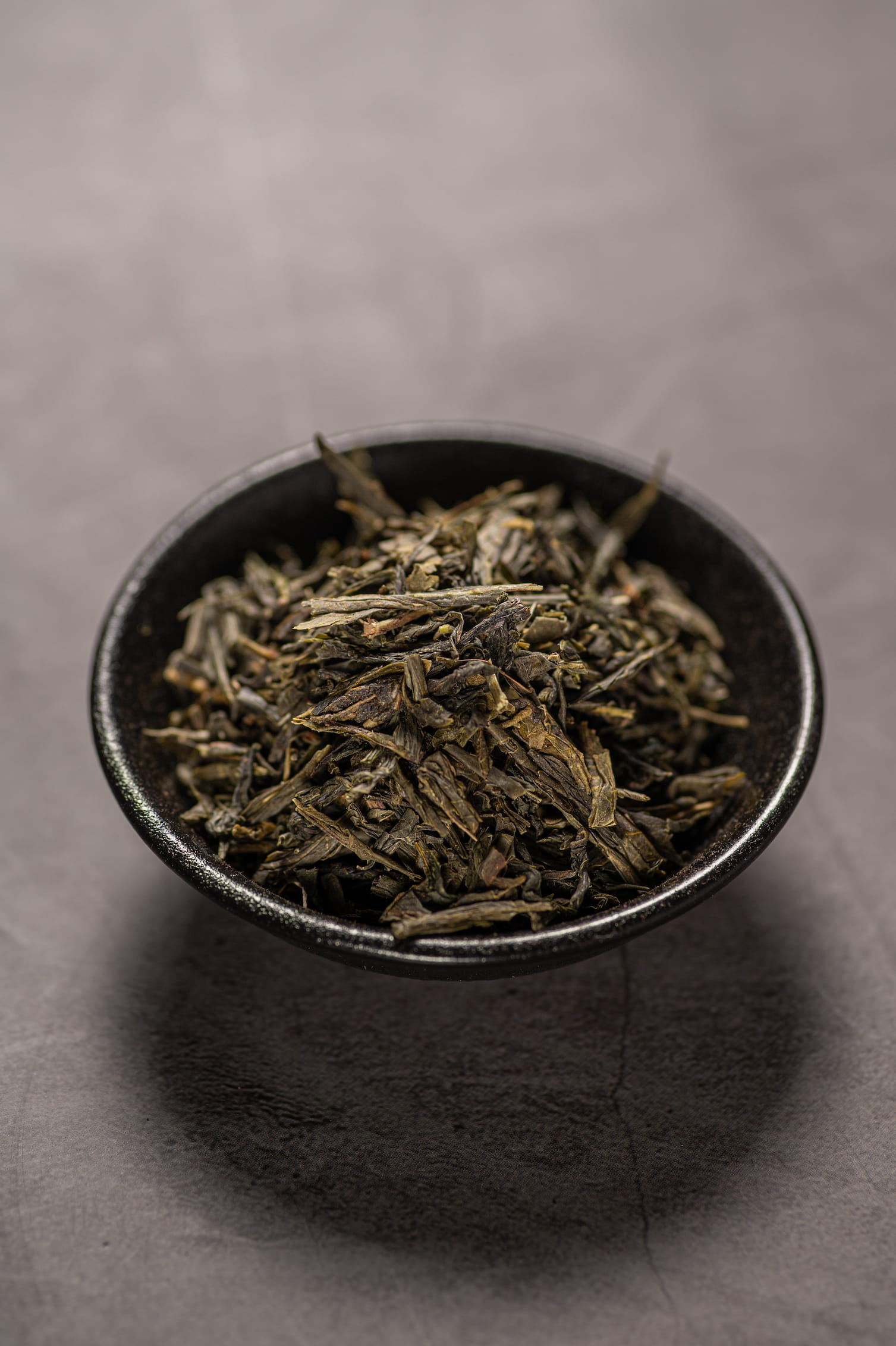 A black bowl filled with dry sencha green tea.