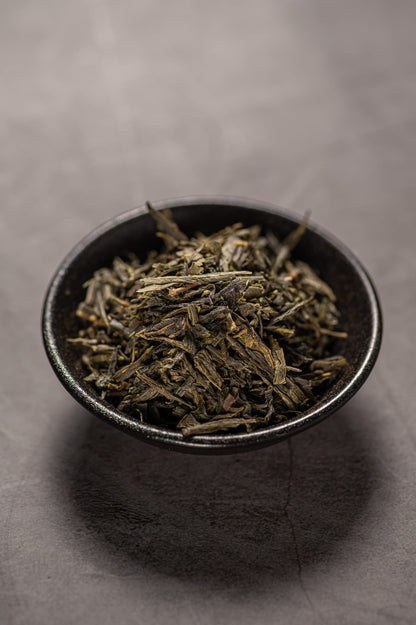 A black bowl filled with dry sencha green tea.